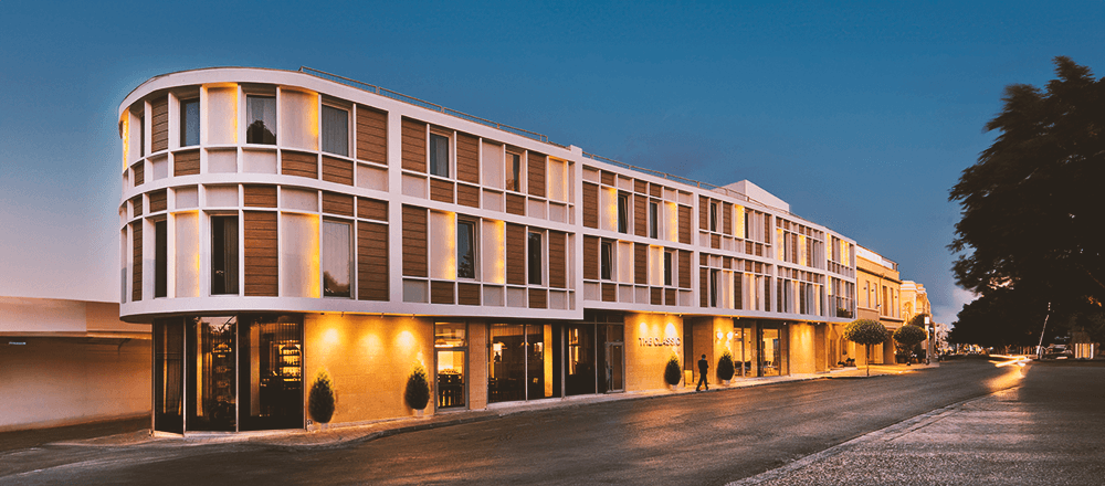 Modern facade of The Classic Hotel in Nicosia, Cyprus, illuminated at dusk with warm lighting and a clear evening sky.